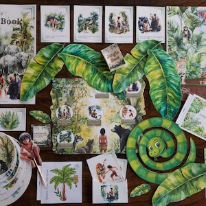 May include: A collection of illustrated items from "The Jungle Book" including a book, cards, and decorative leaves. The book cover features elephants and the title. Other cards depict scenes with animals and characters. A green snake is also present.