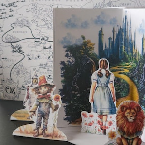 May include: A colorful pop-up book featuring illustrations from The Wizard of Oz. The scene includes Dorothy, the Scarecrow, the Cowardly Lion, and the Emerald City. A map of Oz is visible in the background.