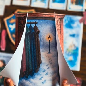 May include: A children's book illustration featuring a winter scene with a lamppost and footprints in the snow. The illustration is framed by a wooden border, with the pages partially open to reveal the artwork. Coats hang on a rack.