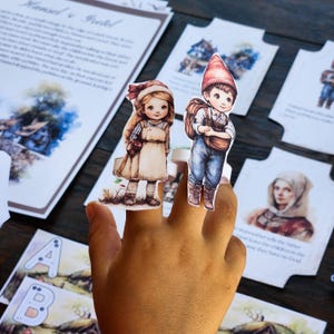 May include: A set of finger puppets featuring a girl and a boy dressed in traditional clothing. The puppets are made of paper and have a watercolour-like design. The girl is wearing a brown dress with a white apron and a red bow in her hair. The boy is wearing a blue shirt, brown trousers, and a red hat. The puppets are being held by a hand.