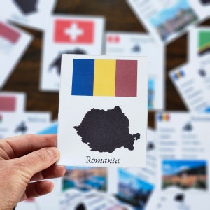 May include: A white card with the flag of Romania and a black outline of the country's shape. The card also includes the word "Romania" printed in black.