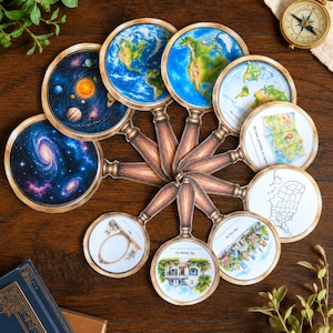 Könnte beinhalten: Eine Sammlung von zehn kreisförmigen Karten in Form von Lupen mit Holzoptik-Griffen, die verschiedene Illustrationen zeigen, darunter eine Galaxie, das Sonnensystem, die Erde, eine Weltkarte, ein Haus, eine Stadt, einen Spiegel und eine US-Landkarte.