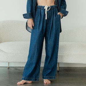 May include: A dark blue denim button-down shirt worn open over a beige cropped tank top, paired with matching dark blue denim wide-leg trousers featuring an elastic waistband and a white drawstring cord, creating a coordinated denim outfit.