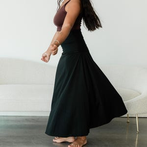 May include: A dark brown sleeveless tank top with a scoop neckline paired with a high-waisted black maxi skirt that features a wide waistband and a flared, flowing silhouette that reaches down to the ankles.