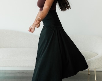 May include: A dark brown sleeveless tank top with a scoop neckline paired with a high-waisted black maxi skirt that features a wide waistband and a flared, flowing silhouette that reaches down to the ankles.