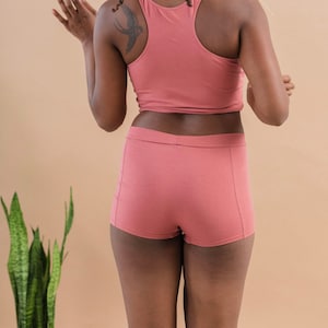 May include: A woman wearing a pink tank top and matching pink shorts. She has a small bird tattoo on her shoulder.