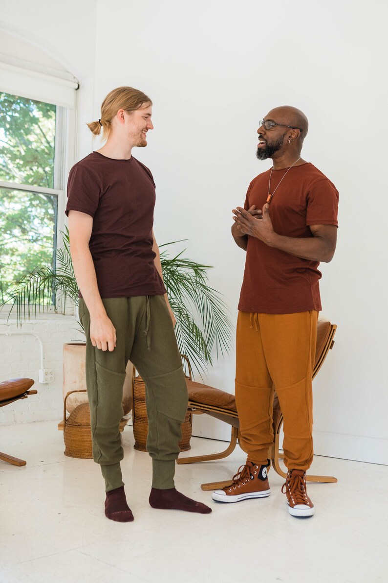 Pu&ograve; includere: Due persone, una con una camicia marrone e pantaloni verdi, l'altra con una camicia marrone e pantaloni arancioni, stanno in piedi uno di fronte all'altro e parlano. Entrambi indossano calze marroni e scarpe da ginnastica marroni.