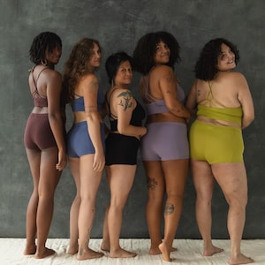 May include: Five people stand in a row, facing away from the camera, wearing different colored underwear. The underwear is all the same style, with a high waist and a wide leg.