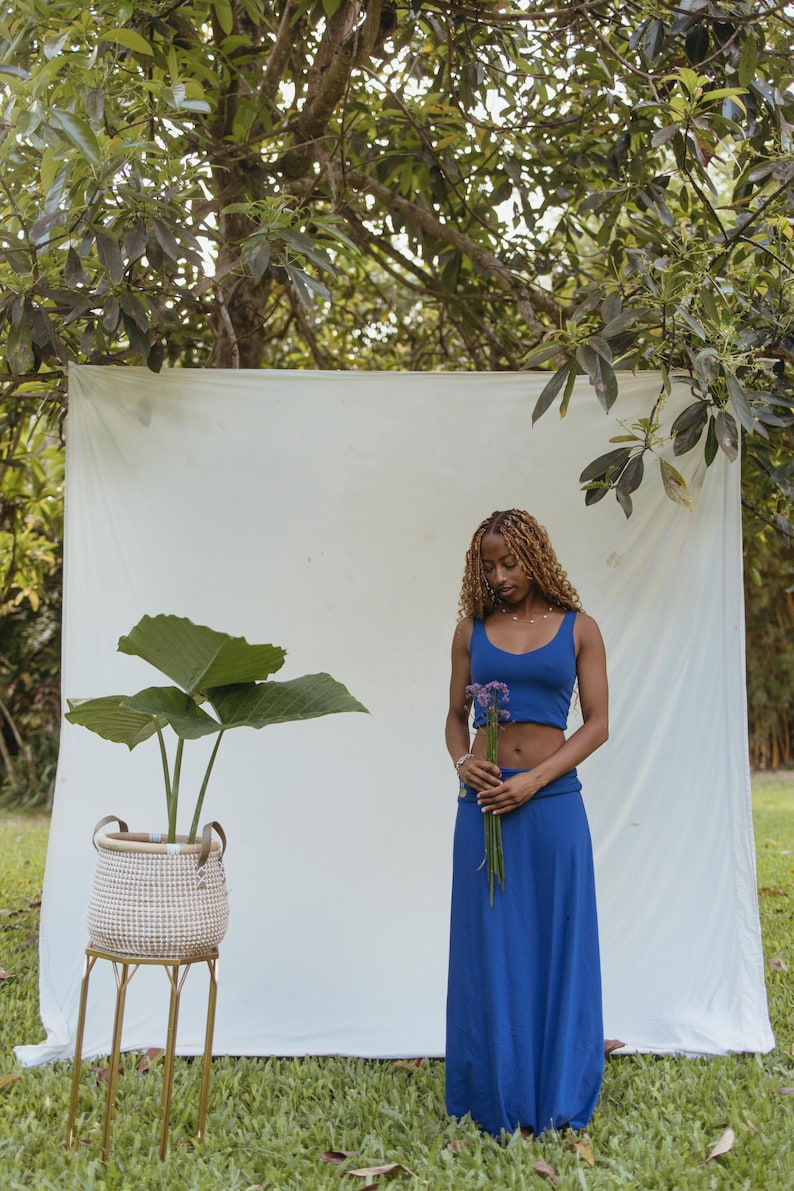 May include: A royal blue two-piece set consisting of a sleeveless cropped tank top and a matching high-waisted maxi skirt. The outfit is a solid, vibrant blue color with a simple, clean design, featuring a fitted top and a long, flowing skirt.