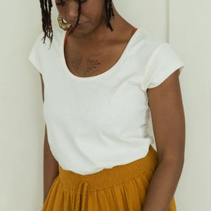 May include: A woman wearing a white scoop-neck t-shirt and mustard-yellow drawstring pants. The t-shirt has short sleeves and a simple design. The pants have a comfortable, relaxed fit. The outfit is casual and suitable for everyday wear.
