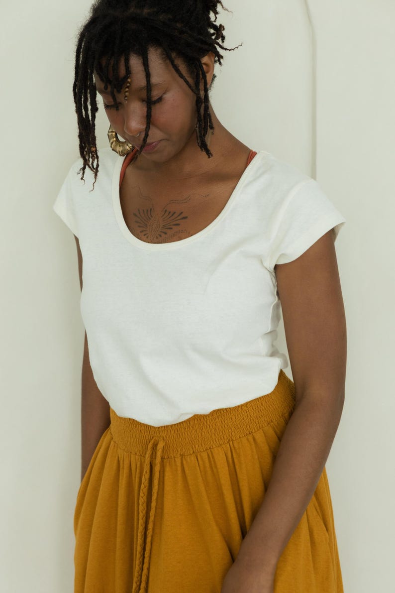 May include: A woman wearing a white scoop-neck t-shirt and mustard-yellow drawstring pants. The t-shirt has short sleeves and a simple design. The pants have a comfortable, relaxed fit. The outfit is casual and suitable for everyday wear.