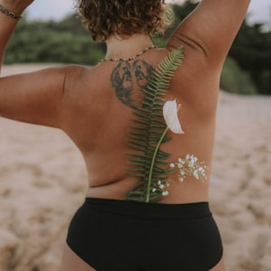 May include: A person wearing black underwear with a fern and white flowers on their back.