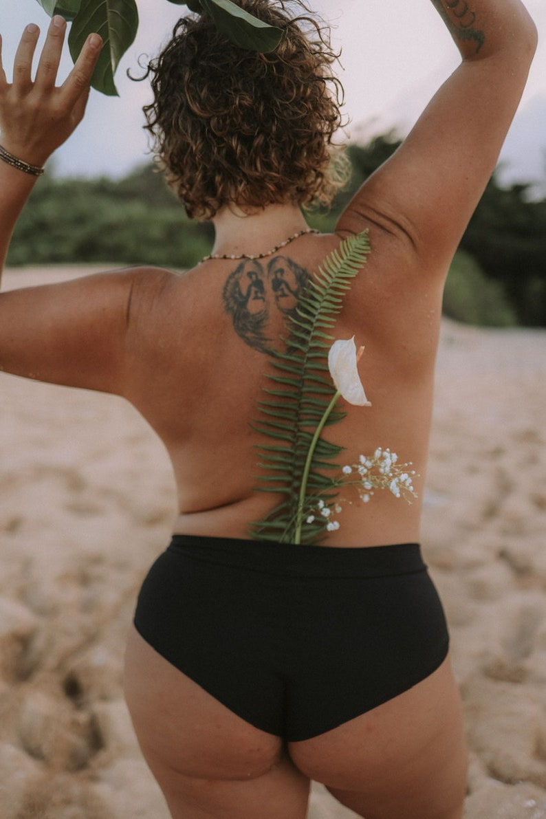 May include: A person wearing black underwear with a fern and white flowers on their back.