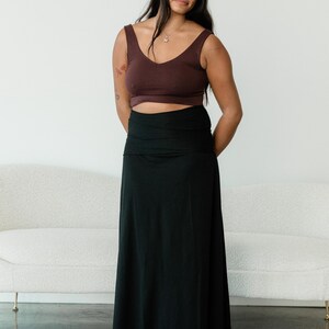 May include: A dark brown sleeveless crop top with a V-neckline paired with a solid black floor-length maxi skirt featuring a wide, folded waistband. The ensemble consists of a fitted upper garment and a long, flowing skirt that reaches the floor.