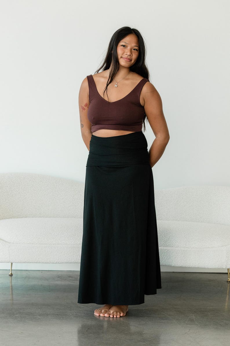 May include: A dark brown sleeveless crop top with a V-neckline paired with a solid black floor-length maxi skirt featuring a wide, folded waistband. The ensemble consists of a fitted upper garment and a long, flowing skirt that reaches the floor.