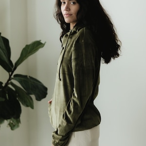 May include: An olive green hoodie with a drawstring and long sleeves, worn with cream corduroy trousers. The outfit is casual and comfortable, suitable for everyday wear.
