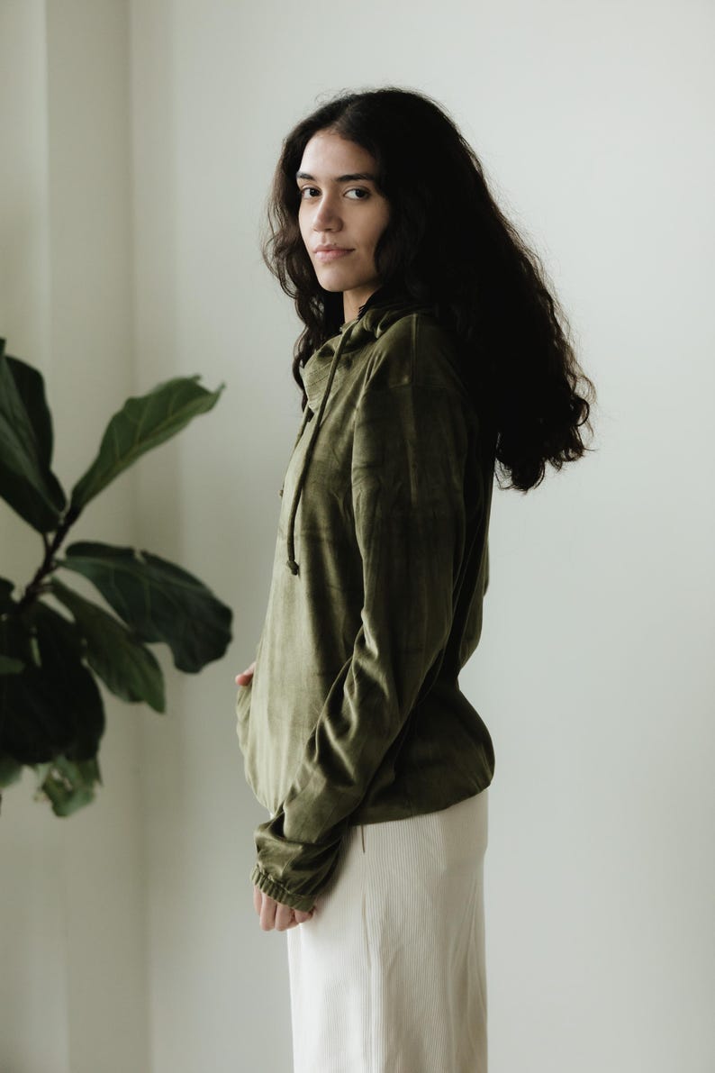 May include: An olive green hoodie with a drawstring and long sleeves, worn with cream corduroy trousers. The outfit is casual and comfortable, suitable for everyday wear.