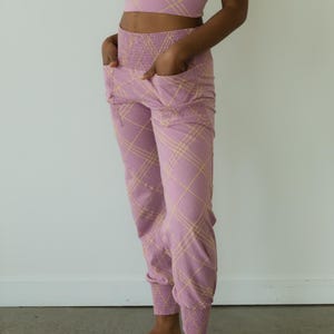 May include: A matching lavender athletic set featuring a sports bra and joggers. The set has a plaid pattern in a lighter yellow color. The joggers have pockets and elastic cuffs at the ankles. The bra has a scoop neck and spaghetti straps.