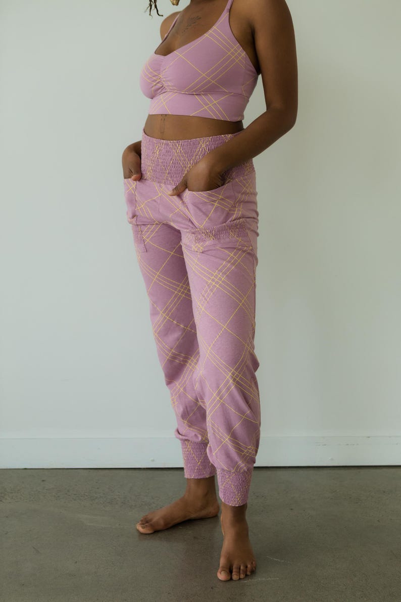 May include: A matching lavender athletic set featuring a sports bra and joggers. The set has a plaid pattern in a lighter yellow color. The joggers have pockets and elastic cuffs at the ankles. The bra has a scoop neck and spaghetti straps.