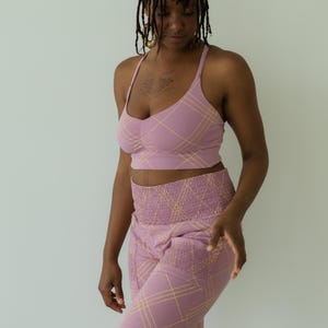 May include: A two-piece lavender outfit with a plaid pattern. The set includes a crop top with thin straps and a high-waisted pair of pants. The plaid design features thin yellow lines. The outfit is made of a soft, comfortable material.