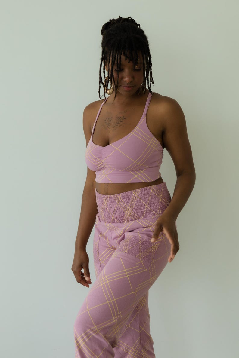 May include: A two-piece lavender outfit with a plaid pattern. The set includes a crop top with thin straps and a high-waisted pair of pants. The plaid design features thin yellow lines. The outfit is made of a soft, comfortable material.