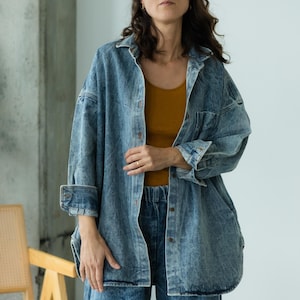 Peut inclure: Une chemise en jean bleu clair et un jean assorti. La chemise a une fermeture boutonnée sur le devant, deux poches poitrine et des manches longues. Le modèle porte un débardeur de couleur moutarde en dessous. La tenue est décontractée et élégante.