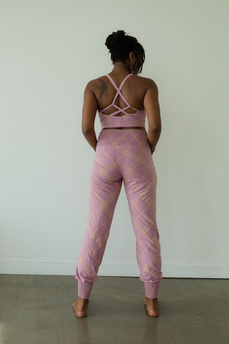 May include: A matching activewear set in a light purple hue with a plaid pattern in a lighter shade. The set includes a sports bra with crisscross straps and high-waisted pants with elastic cuffs.