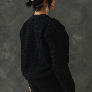 May include: A black knitted sweater with a textured pattern. The sweater has long sleeves and a v-neck.