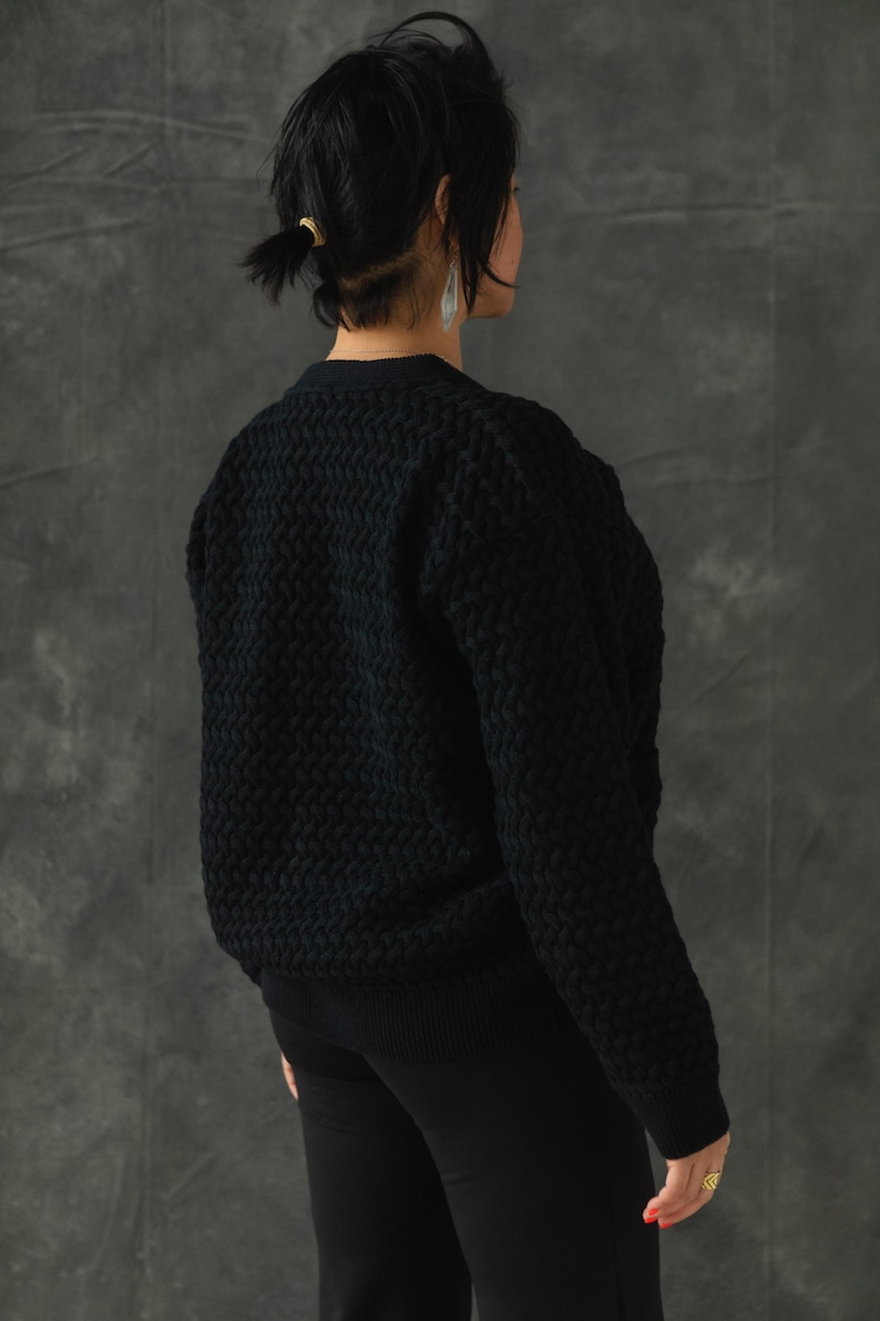 May include: A black knitted sweater with a textured pattern. The sweater has long sleeves and a v-neck.