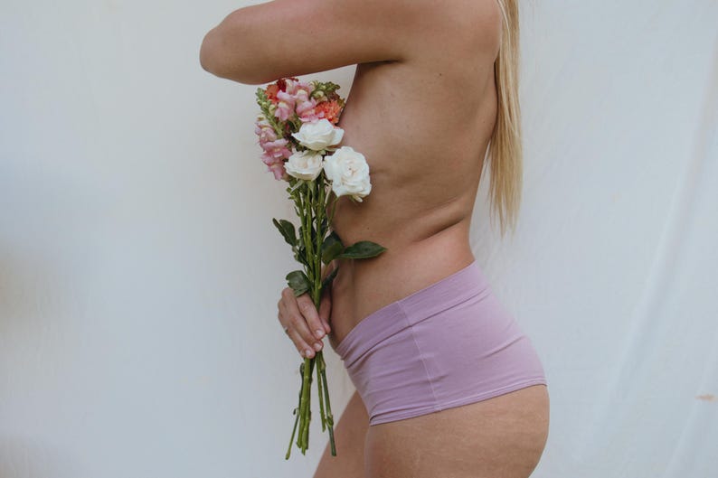 May include: A bouquet of flowers with white, pink, and orange blooms is held against a person's side. The person is wearing lavender shorts. The background is a plain white.