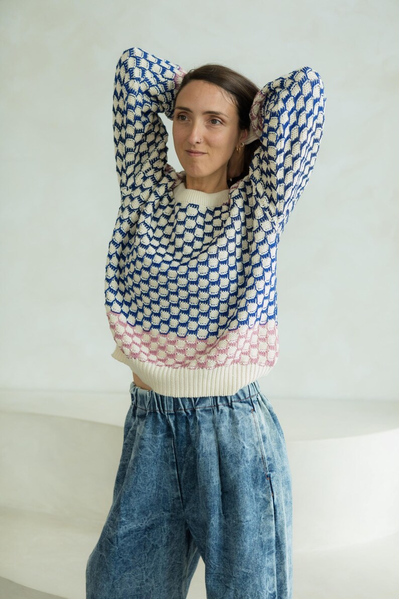 May include: A patterned sweater with a white base, blue and white geometric design, and a pink and white striped hem. The sweater is paired with acid wash denim jeans.