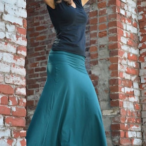 May include: A solid black short-sleeved t-shirt with a V-neckline paired with a floor-length teal maxi skirt. The skirt features a wide, smooth waistband and a flared, flowing silhouette that extends down to the ankles, made of a plain fabric.