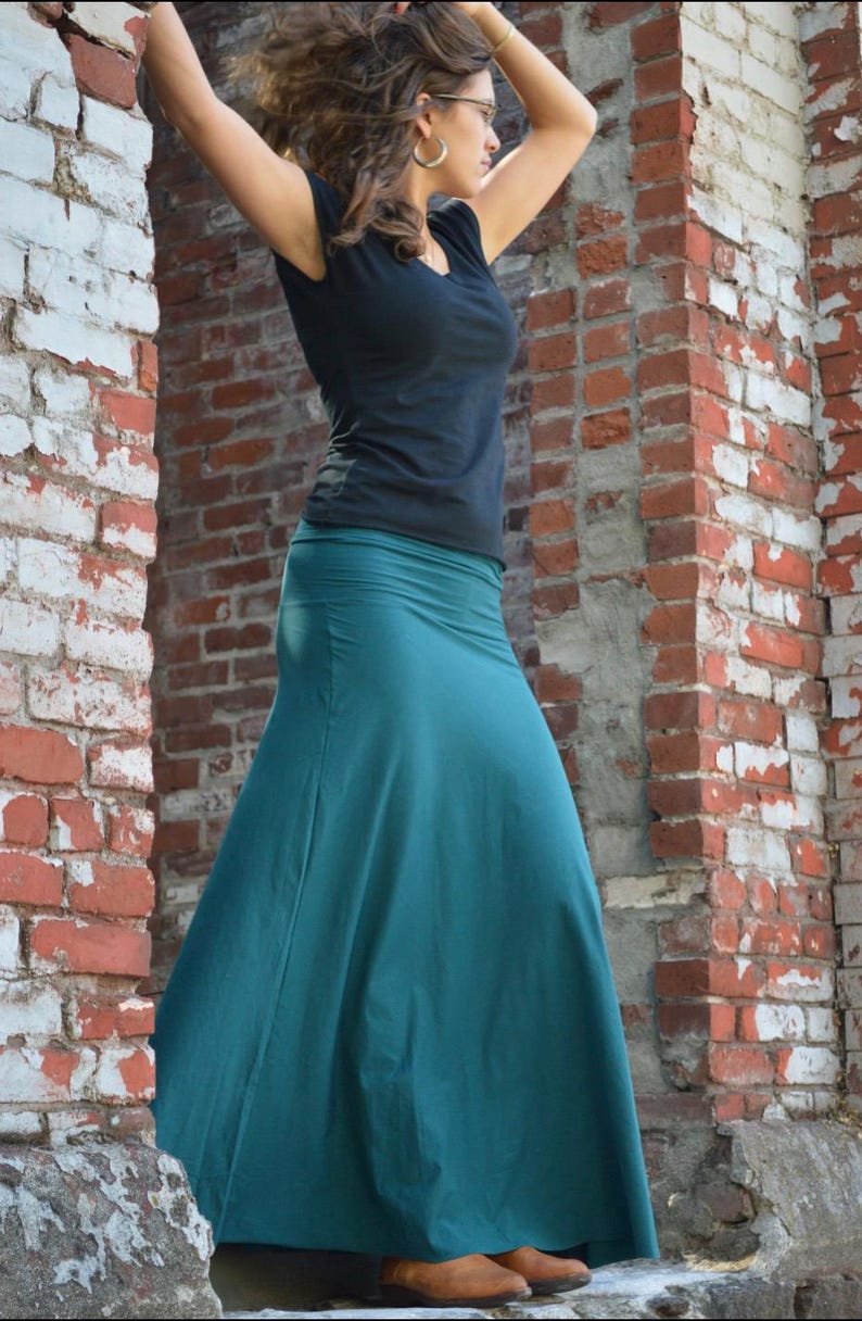 May include: A solid black short-sleeved t-shirt with a V-neckline paired with a floor-length teal maxi skirt. The skirt features a wide, smooth waistband and a flared, flowing silhouette that extends down to the ankles, made of a plain fabric.