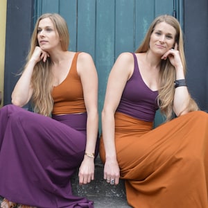 May include: Two sleeveless tank tops and two long maxi skirts in solid rust orange and deep purple colors. One outfit features a rust orange tank top with a purple maxi skirt, while the other features a purple tank top with a rust orange maxi skirt.
