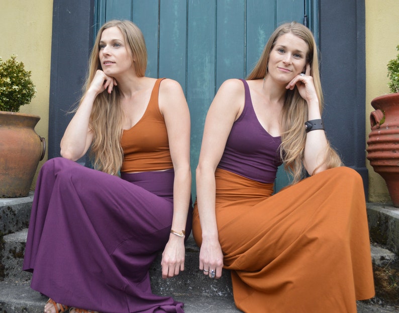 May include: Two sleeveless tank tops and two long maxi skirts in solid rust orange and deep purple colors. One outfit features a rust orange tank top with a purple maxi skirt, while the other features a purple tank top with a rust orange maxi skirt.