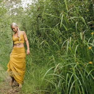 May include: A mustard yellow two-piece set consisting of a cropped tank top with a gathered neckline and a matching floor-length maxi skirt with a wide, fitted waistband. The fabric is a solid, matte mustard yellow color throughout the garment.