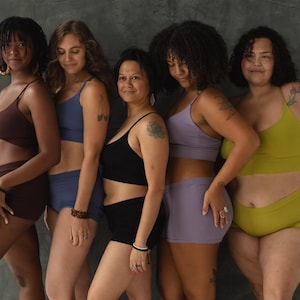 May include: Five women wearing different colored underwear sets. The underwear is made of a soft, stretchy fabric and has a comfortable fit. The women are standing in front of a gray wall.