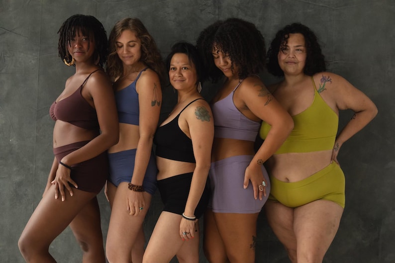 May include: Five women wearing different colored underwear sets. The underwear is made of a soft, stretchy fabric and has a comfortable fit. The women are standing in front of a gray wall.