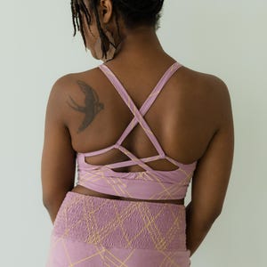 Peut inclure: Ensemble de sport mauve compos&eacute; d'un soutien-gorge de sport crois&eacute; et d'un legging taille haute, tous deux avec un motif quadrill&eacute; jaune. Le soutien-gorge a un design arri&egrave;re unique. Le legging a une taille fronc&eacute;e. Un tatouage d'oiseau est visible.