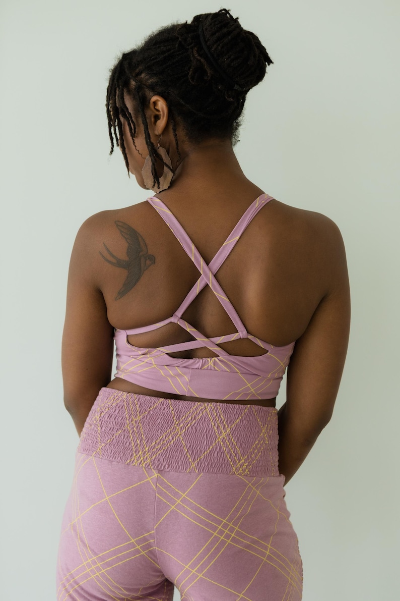 Peut inclure: Ensemble de sport mauve compos&eacute; d'un soutien-gorge de sport crois&eacute; et d'un legging taille haute, tous deux avec un motif quadrill&eacute; jaune. Le soutien-gorge a un design arri&egrave;re unique. Le legging a une taille fronc&eacute;e. Un tatouage d'oiseau est visible.