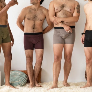 Puede incluir: Cuatro hombres con calzoncillos de diferentes colores. Los calzoncillos son todos de un estilo similar, con una cintura ancha y un ajuste holgado. Los hombres est&aacute;n de pie frente a una pared blanca.