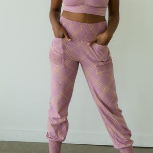 May include: A matching set of athletic wear in a mauve color with a yellow plaid pattern. The set includes a sports bra and joggers. The joggers have pockets and elastic cuffs at the ankles.