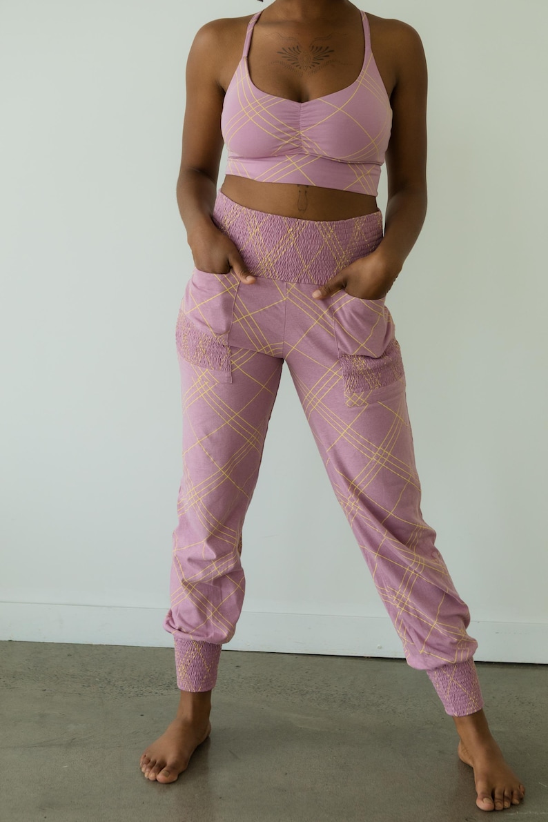 May include: A matching set of athletic wear in a mauve color with a yellow plaid pattern. The set includes a sports bra and joggers. The joggers have pockets and elastic cuffs at the ankles.