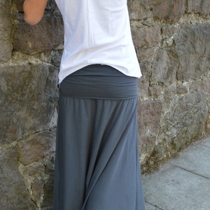 May include: A white short-sleeved t-shirt with a V-neckline paired with a dark gray maxi skirt featuring a wide, fold-over waistband. The skirt has a long, flowing silhouette that reaches toward the ground, made of a solid-colored fabric.