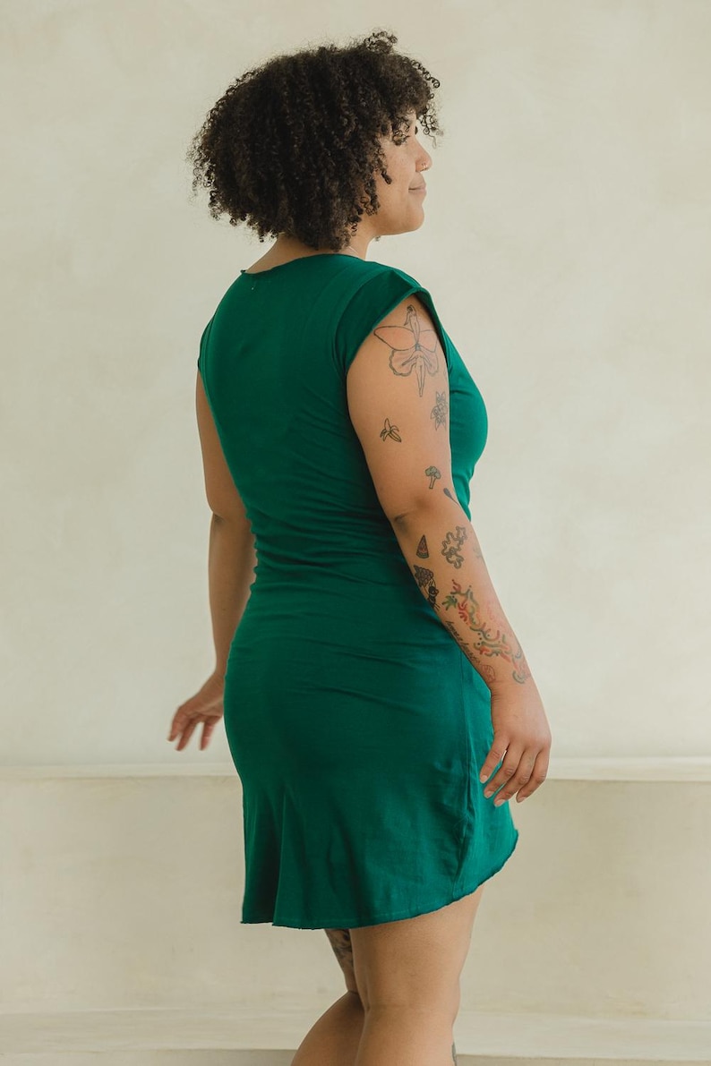 May include: A solid dark green short-sleeved dress with a round neckline and a fitted silhouette that extends to the mid-thigh. The garment features a simple, clean design with a smooth texture and a straight hemline, captured from a side profile view.