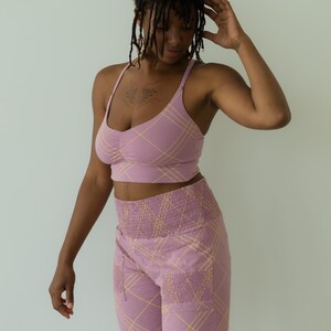 May include: A matching set of lilac-colored activewear. The set includes a crop top with thin straps and high-waisted pants. Both pieces feature a yellow plaid pattern. The pants have pockets and a ruched waistband.