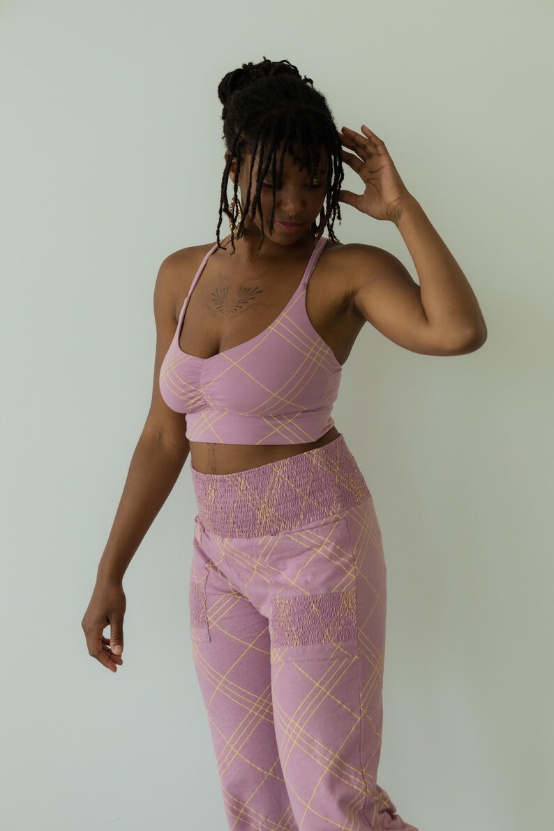 May include: A matching set of lilac-colored activewear. The set includes a crop top with thin straps and high-waisted pants. Both pieces feature a yellow plaid pattern. The pants have pockets and a ruched waistband.