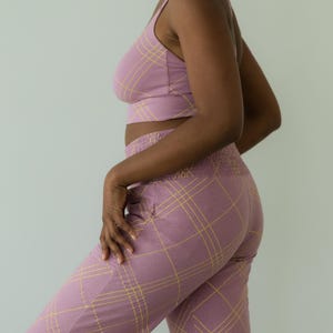 May include: A matching set of lilac-colored clothing with a yellow plaid pattern. The set includes a crop top with spaghetti straps and high-waisted pants. The pants have a smocked waistband and pockets.