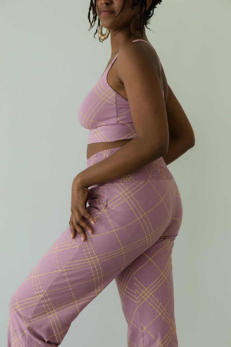 May include: A matching set of lilac-colored clothing with a yellow plaid pattern. The set includes a crop top with spaghetti straps and high-waisted pants. The pants have a smocked waistband and pockets.