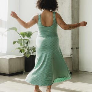 May include: A sleeveless dress featuring a scoop neckline and a flared skirt, crafted from a light green and dark green striped fabric. The garment has a fitted bodice that transitions into a flowing, diagonal-striped skirt that reaches mid-calf.